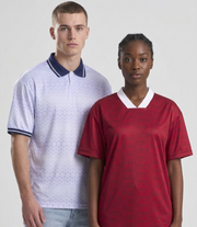 Male and female models standing together against a light gray background, both wearing patterned short-sleeved retro sports jerseys. The male model on the left is wearing a light purple to white gradient jersey with a blue and white striped polo collar and cuffs. The female model on the right is wearing a red geometric patterned jersey with a white v-neck collar. Both face forward with serious expressions.
